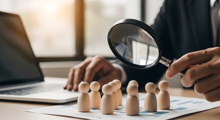 Fototapeta premium Businessman Using Magnifying Glass to Inspect Wooden Figures for Recruitment and Human Resources Concept