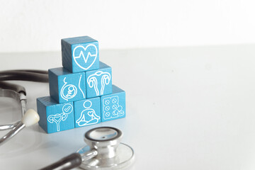 Pyramid of blue wooden blocks with women health icons: heart, pregnancy, uterus, yoga, and pills near stethoscope on white background. Gynecology, reproductive system, and wellness concept.
