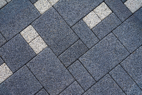 Dark gray paving tiles with speckled gravel texture and diagonal layout, accented by light tiles. Concept of paving tiles, textured surfaces, modern design background