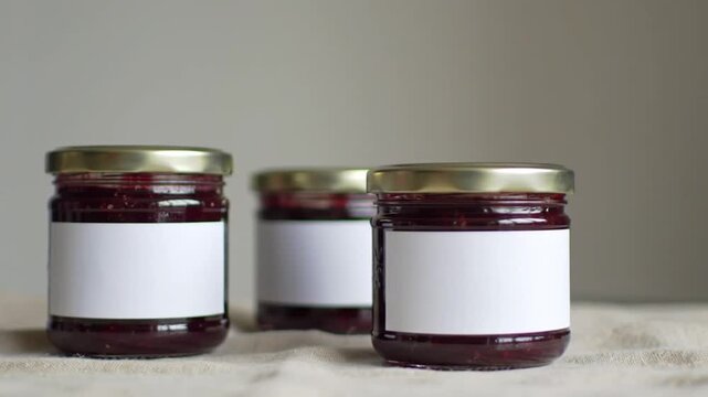 Three glass jars filled with homemade berry jam sit on a textured cloth, ready for labeling.