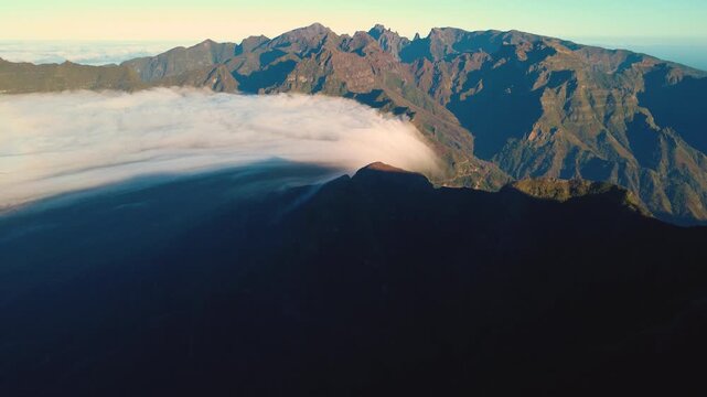 Establishing shot of a rare cloud waterfall over Sao Vicente valley in Madeira, aerial view of white clouds flowing through green mountains like a river under bright sun from Bica da Cana, epic.