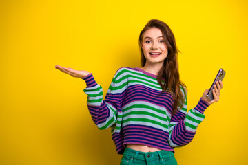 Young woman model wearing striped pullover posing with smartphone against bright yellow background...