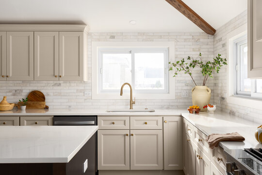 A kitchen detail with brown cabinets, marble subway tile backsplash,gold faucet, and decorations on the marble countertop.