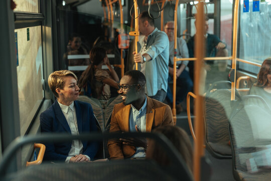 Two professionals share a friendly conversation on a city bus during urban commute