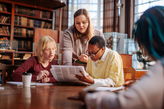 Students collaborate in a quiet library, studying together and discussing a newspaper during a group learning session
