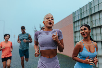 Fototapeta premium Group of friends enjoying a lively outdoor fitness run with smiles and energy in the city