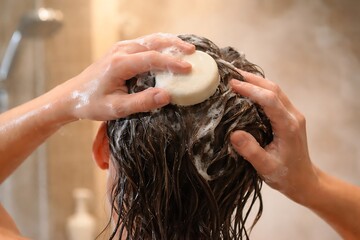 Naklejka premium Close-up of Woman Washing Hair with Solid Shampoo Bar in Shower