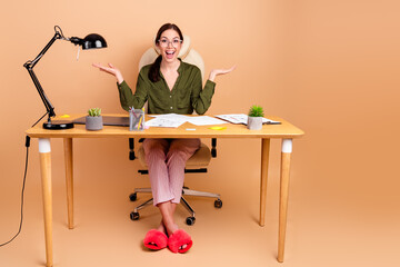 Young businesswoman sits at desk smiling widely in chic office setup with beige background