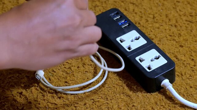Close up of hand plugging white power adapter into black power strip with USB-C cable