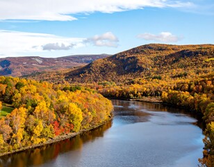 A vibrant autumn landscape features a meandering river flowing through colorful trees and rolling hills under a bright blue sky with wispy clouds