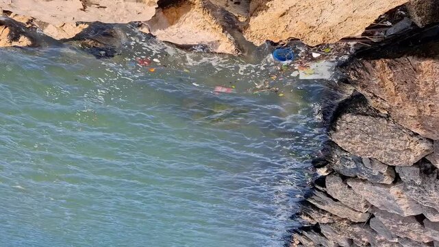 Trash and waste items float in the water near a rocky shoreline. This shows how human activity affects the health of the ocean and its ecosystems.