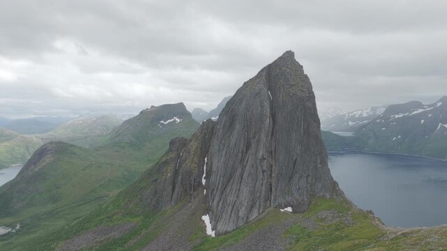 Aerial, slow forward drone flight towards impressive peak and cliff of famous Segla on Senja island during cloudy summer day. Amazing hiking destination, outdoor adventure. Fjords and mountains.