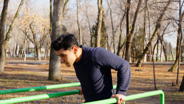 Fit guy doing push ups on parallel bars in park