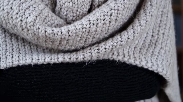 Close-up of a person wearing a cozy, light grey knitted sweater, showcasing the intricate texture and warmth of the fabric, perfect for cold weather.