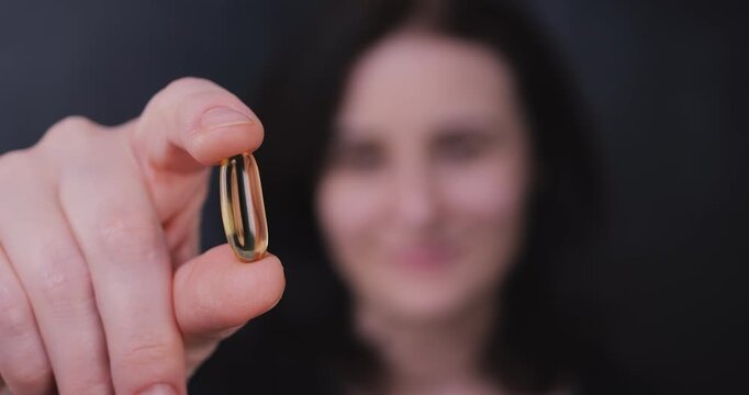 Adult woman holding an omega-3 pill toward the camera, highlighting heart health, supplements, self-care, and overall wellness.