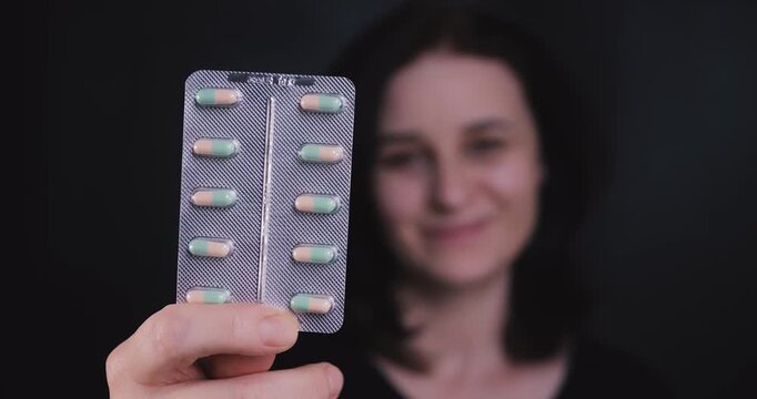 Adult woman holding a blister of pills toward the camera, representing health, pharmacy, menopause care, and dietary supplements concept.
