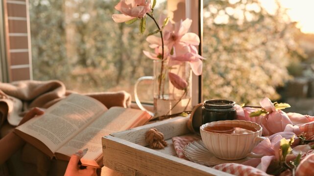 Cozy morning reading with tea and blooming magnolia flowers by the window