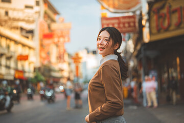 Happy Asian woman smiling and walking in Bangkok Chinatown (Yaowarat). Young female traveler enjoying street food atmosphere with Chinese signs background. Outdoor lifestyle travel and tourism concept