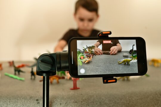 Child filming stop motion animation with dinosaur toys on a table using a smartphone
