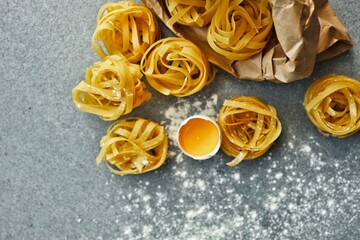Fresh fettuccine nests and a cracked egg yolk on a floured stone surface