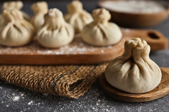 Uncooked khinkali dumplings arranged on a wooden board dusted with flour
