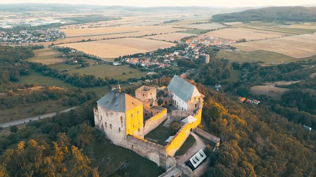 Discover Tocnik Castle, a stunning medieval ruin perched on a hilltop, basking in the warm glow of sunset. Experience the beauty of the surrounding landscape in summer.
