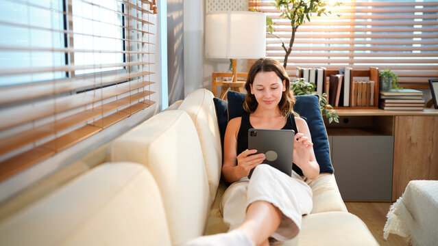 Woman relax on couch with tablet, online streaming with internet and reading ebook or watching film at home. Happy female person with technology, subscription and mobile app with break in living room