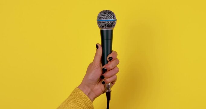 Close-up of a hand holding a microphone against a bright yellow background. Concept of public speaking, music performance, podcasting, interviews, and media communication. Isolated, high contrast, 4K 