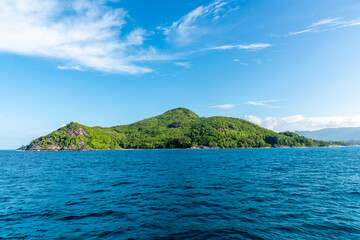 Tropical Islet Covered in Green Vegetation Seen from the Sea under Blue Sky