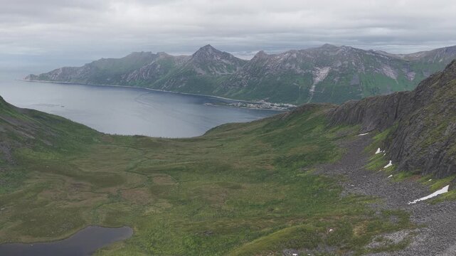 Aerial, forward drone flight above mountains, fjords in distance, rainy summer day.  Hus&oslash;y island, village far away in &Oslash;yfjorden fjord, Senja. Amazing outdoor travel destination, hiking area in Norway