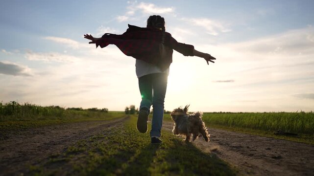 Running with dog on dirt road, person spins arms wide toward sunset over field, silhouette against sky, running dog in rural landscape, freedom and friendship visible, outdoor leisure in golden light