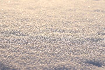 Snowy background with selective focus. The surface is covered with snow, snowflakes sparkling in the sun. The snowy surface shines in the sun, blurred background. Winter background. Cold season