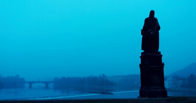 Dark winter morning details of historic statues on Charles Bridge in Prague. Moody blue tones and cold atmosphere create a dramatic and mysterious European city scene.