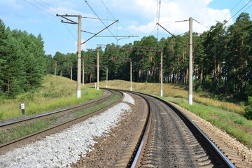 Curved Railway Tracks Through a Green pine Forest with electic pylons in sunny day