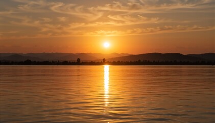 Golden sunset over a lake with mountain silhouette. Orange sky reflecting on water surface. Nature landscape background