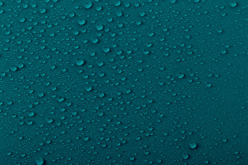 Water drops on a dark teal surface create a pattern showing reflections and shapes in the light during a quiet moment