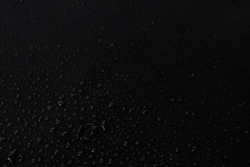 Water droplets scatter on a dark surface after rain, creating a shiny appearance and reflecting light during the early morning