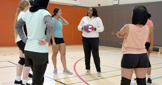 African American coach instructing volleyball team after semicircle in gym gesturing ball for drill
