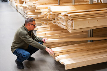 Man selecting timber or checking quality of construction lumber in hardware store