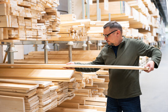 Man selecting timber or checking quality of construction lumber in hardware store