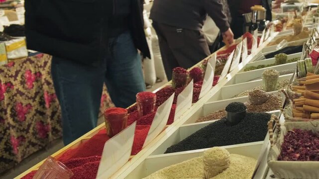 Market spice stall with colorful bins, shoppers browsing rows of grains, beans and spices textured mounds of pepper and cinnamon sticks, wooden scoops and jars on display, patterned fabric backdrop