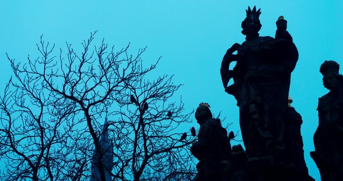Dark winter morning details of historic statues on Charles Bridge in Prague. Moody blue tones and cold atmosphere create a dramatic and mysterious European city scene.