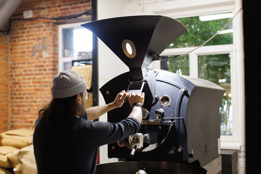 Worker using large industrial roaster machine for roasting coffee