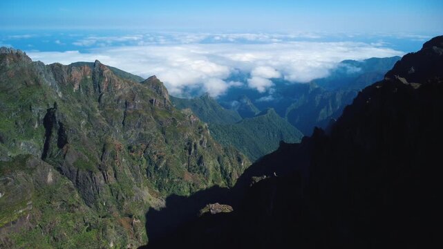 Aerial sideways reveal of PR1 Vereda do Areeiro hiking trail with Stairway to Heaven, drone opening view of tiny hikers on mountain cliffs and Ninho da Manta balcony above the clouds in Madeira.
