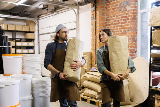 Worker looking at and listening colleague while carrying coffee beans