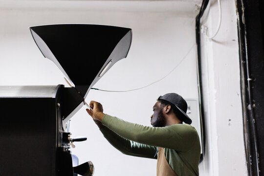 Side view of worker controlling process of coffee beans roasting