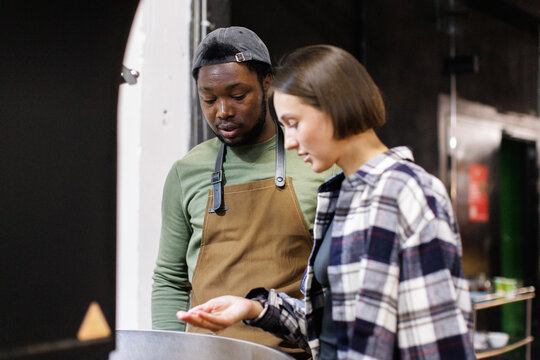 Focused male and female workers controlling process of coffee roasting