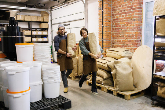 Young female and male workers carrying packages with coffee beans