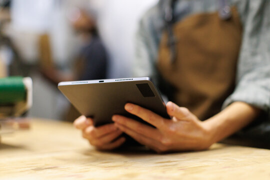 Close up of partial female worker using digital tablet at wooden table