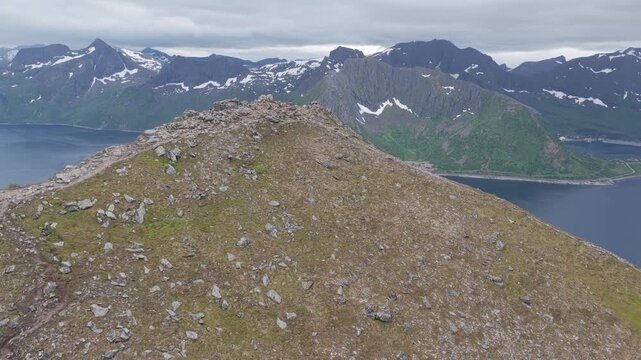 Aerial, forward drone flight above Hesten peak mountain, revealing Medfjorden fjord, rainy summer day. Amazing outdoor travel destination, hiking area in Norway. Wild nature in arctic Norway.
